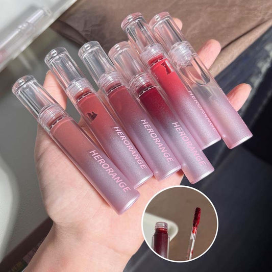 Hand holding six Herorange lip glosses with close-up of two lip glosses.